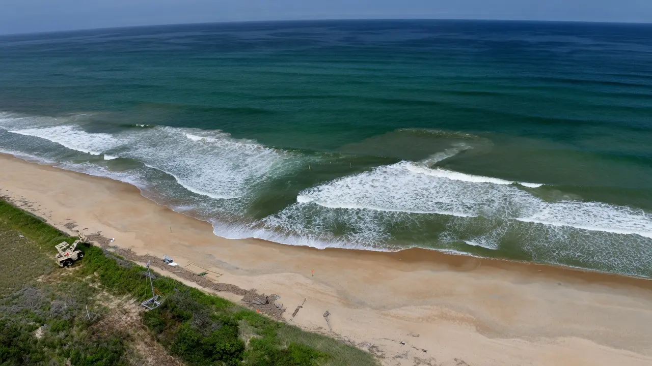 Aerial view of a rip current channel visible as darker calm water between breaking waves
